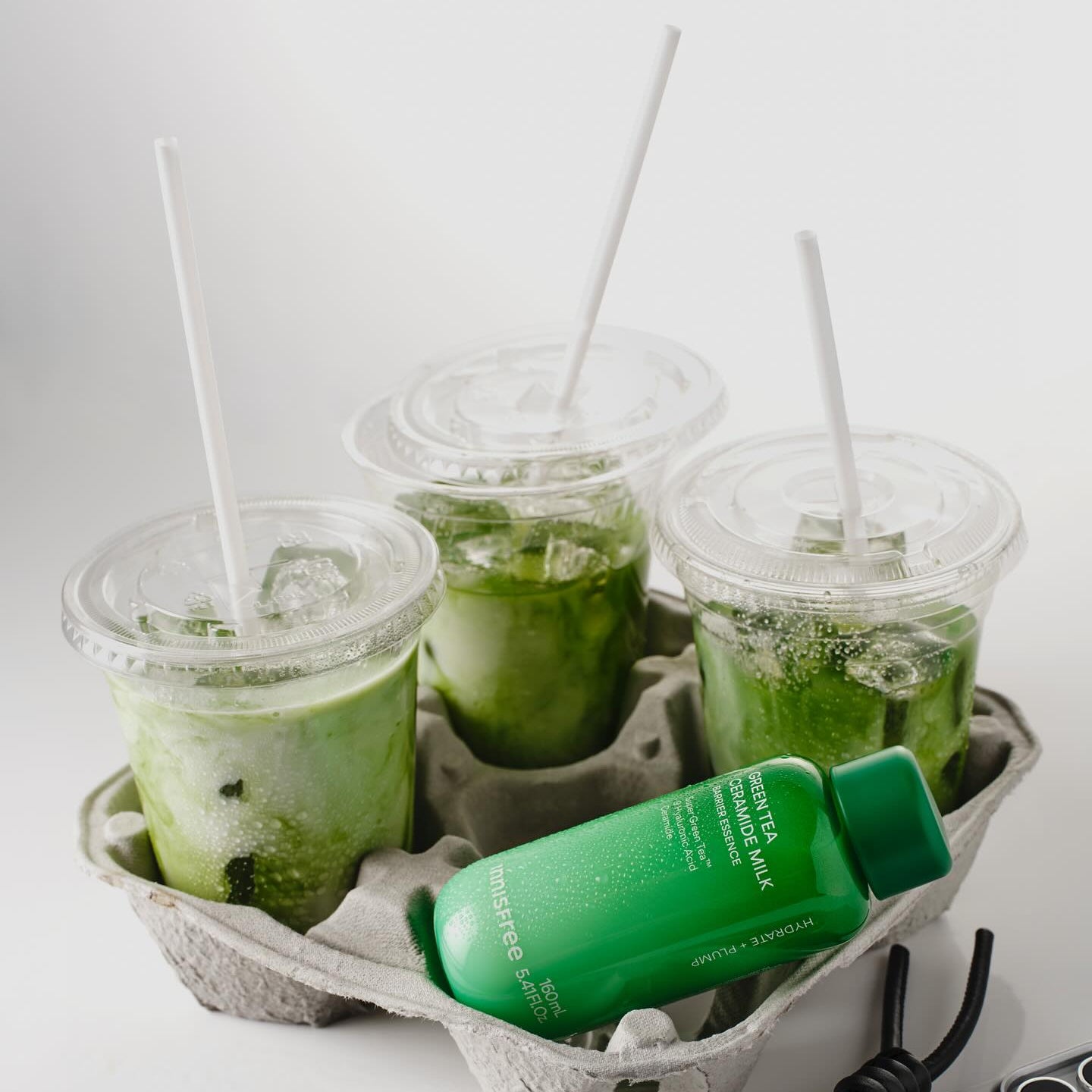 INNISFREE Green Tea Ceramide Milk Essence 160ml, flacon vert sur plateau avec boissons matcha, style promo en studio