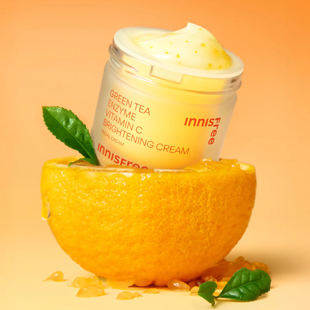 INNISFREE Vitamin C Enzyme Brightening Cream 50ml de la marque Innisfree, pot crème sur agrume et feuilles, fond orange.