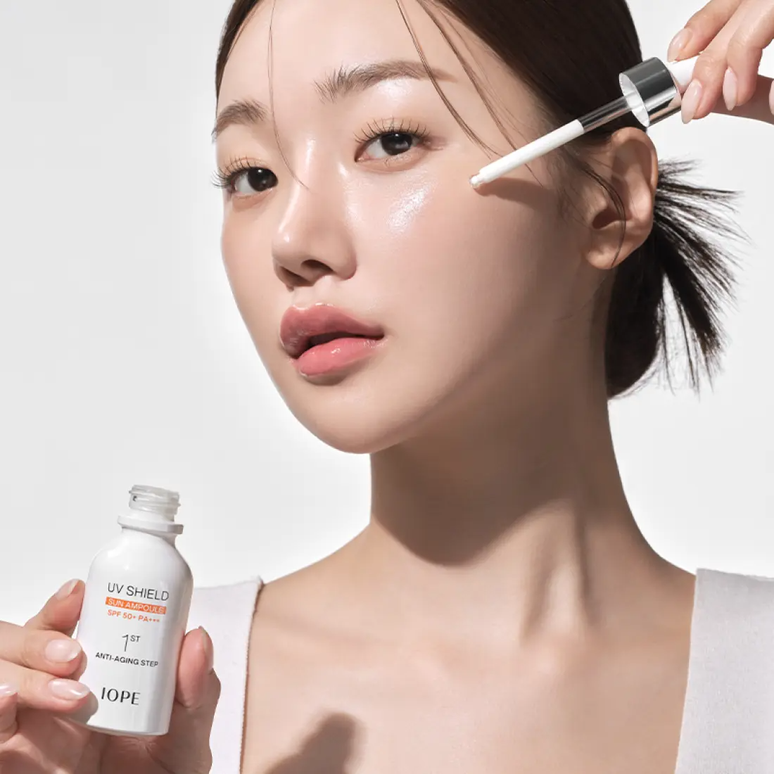 IOPE UV Sheild Sun Ampoule SPF 50+PA+++ 40ml, femme applique le sérum anti-UV sur le visage, contexte beauté