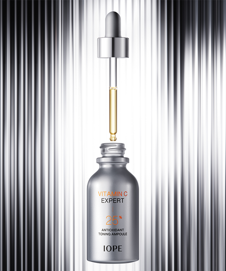 Flacon de IOPE Vitamin C Expert 25% Toning Ampoule 23ml avec pipette, sur fond argenté.
