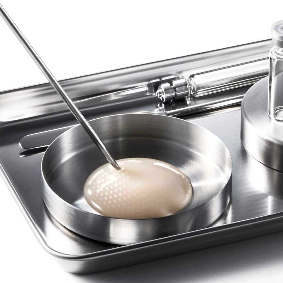 Décris l'image en français : IOPE XMD Stem3 Clinic Recoery Serum 50ml, fiole sur plateau clinique inox, ambiance laboratoire.