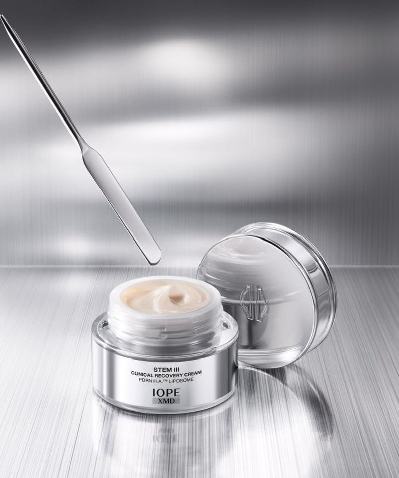 IOPE XMD Stem3 Clinical Recovery Cream 50ml, pot crème et couvercle ouverts sur fond métallique, vue produit en gros plan.