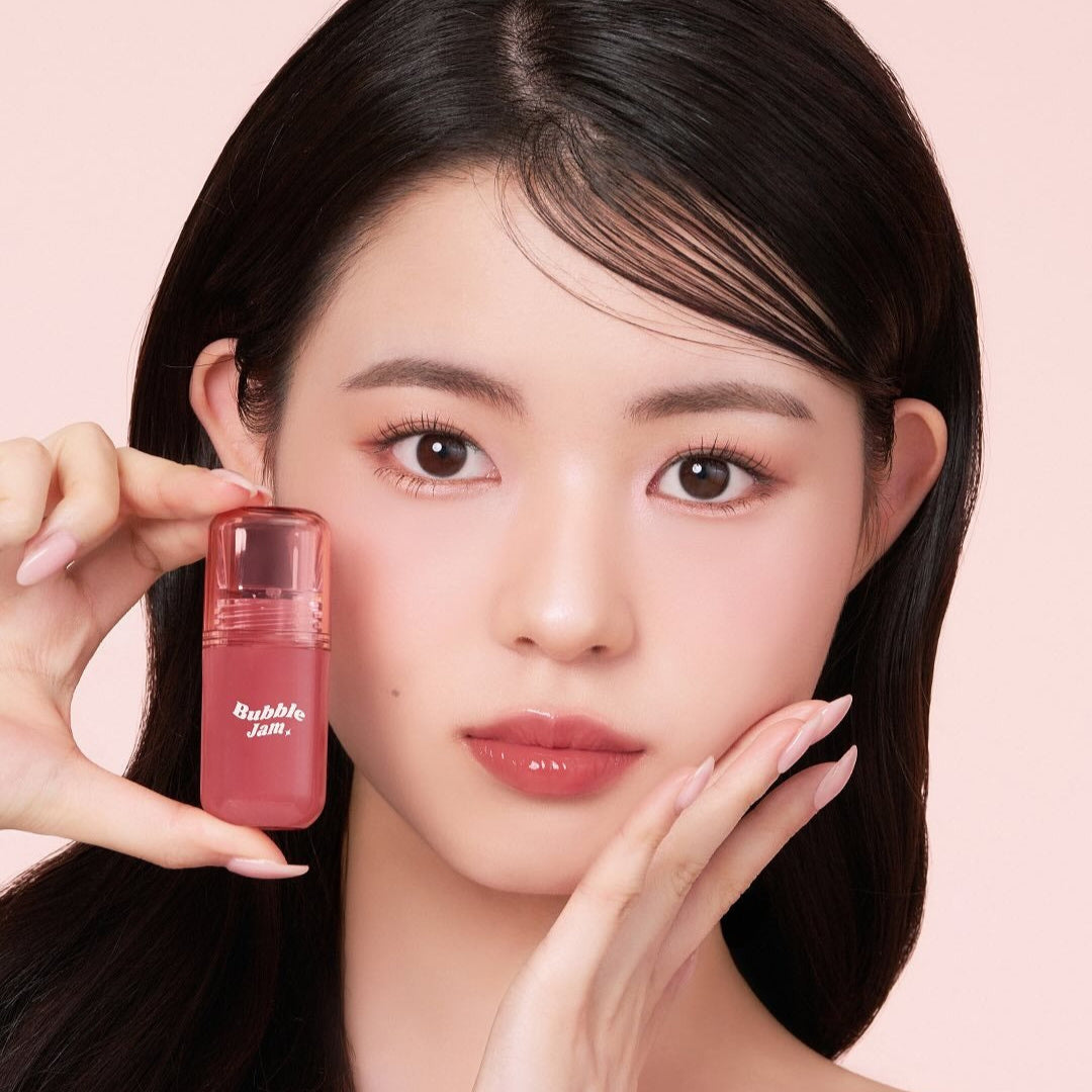 IPKN Bubble Jam Gloss : flacon rose tenu par un mannequin, maquillage lèvres brillantes, fond rose pastel.