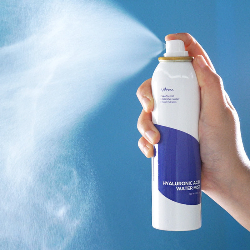 Main tenant ISNTREE Hyaluronic Acid Water Mist 100ml, brume hydratante sur fond bleu, produit de soins visage ISNTREE.
