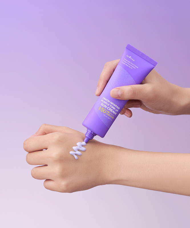 ISNTREE Onion Newpair Purple Tone-Up Sunscreen 50ml, main appliquant une crème violette sur la peau, fond violet.