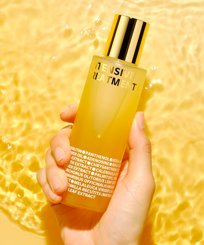 IS0I Intensive Treatment Essence 130ml ISOI, flacon doré tenu main sur fond jaune lumineux, soin visage.