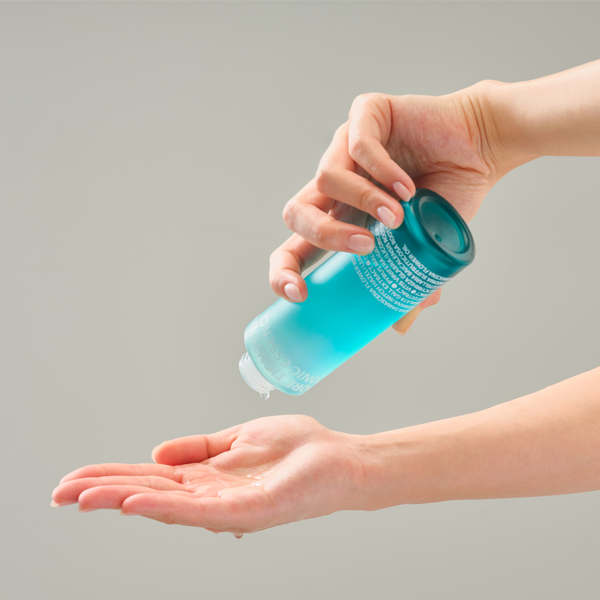 Main tenant ISOI Pore Tightening Tonic Essence 130ml, marque ISOI, application sur peau avec effet tonique bleu, fond clair.
