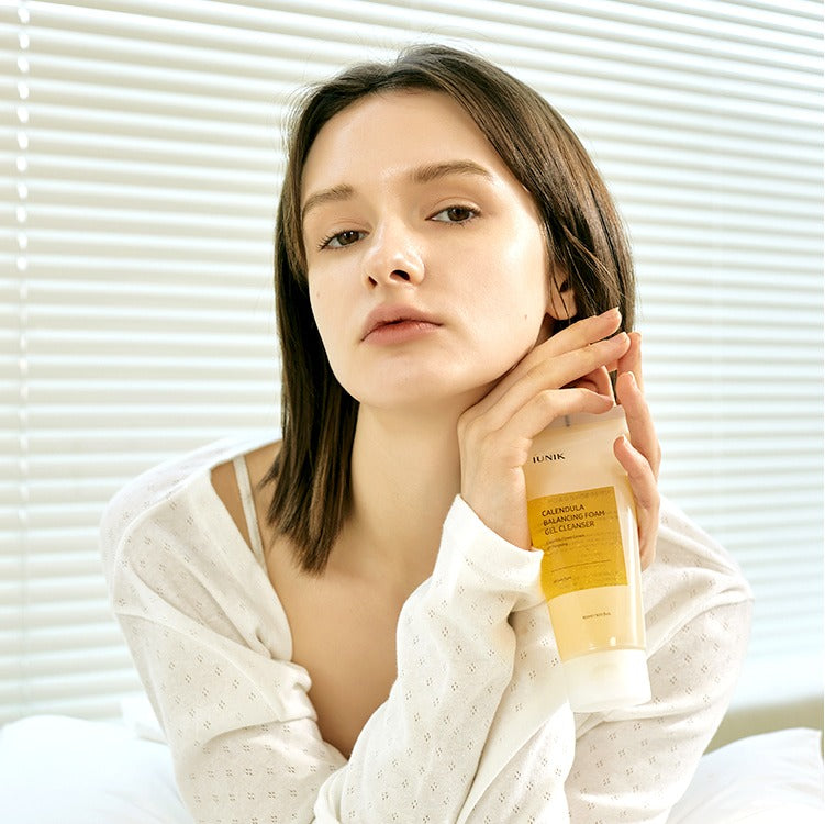 Portrait femme, posant près du produit IUNIK Calendula Balancing Foam Gel Cleanser 150ml de la marque IUNIK, ambiance studio.