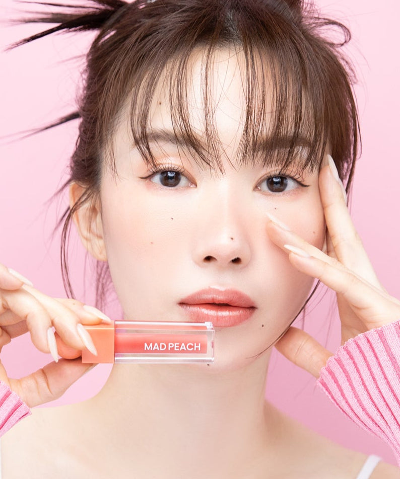 Portrait beauté : IVI MAD PEACH Glow Fit Mood Gloss, maquillage pêche brillant de la marque IVI, fond rose et lumière douce.