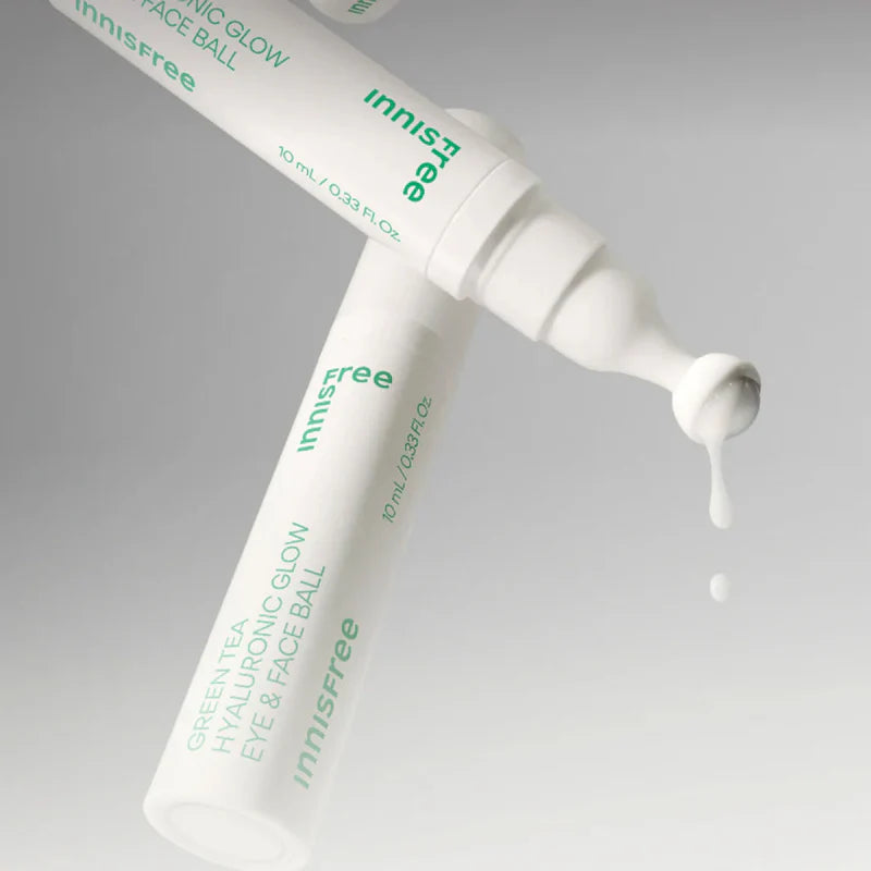 Décris l'image en français : INNISFREE Green Tea Hyaluronic Glow Eye & Face Ball, tube crème vert sur fond clair, gouttes.