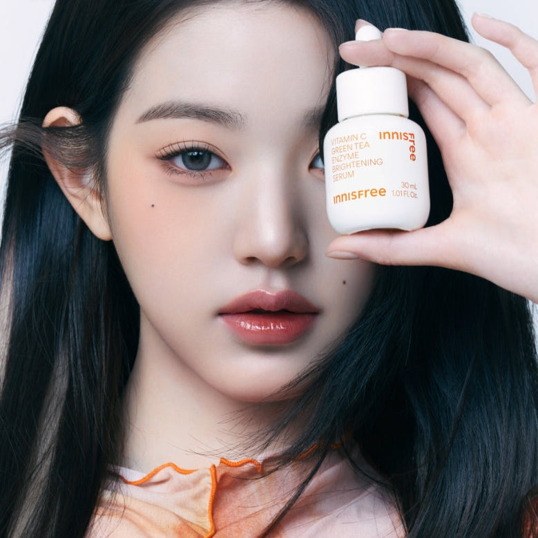 Portrait visage tenant INNISFREE Vitamin C Green Tea Enzyme Brightening Serum, marque INNISFREE, sérum éclat en main