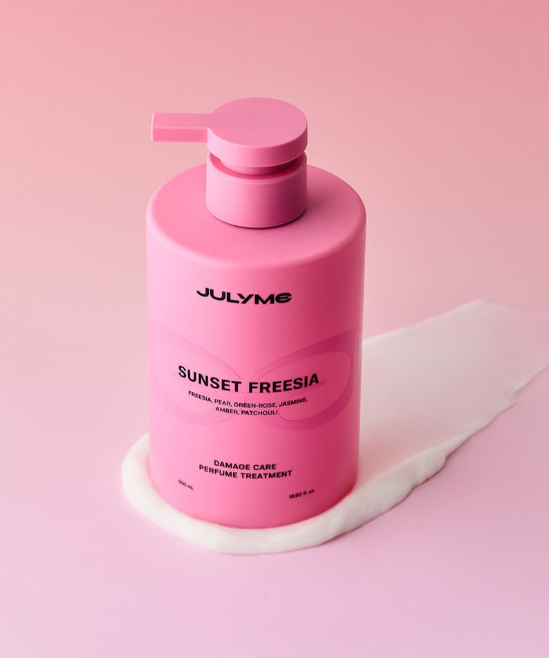 JULYME Damage Care Perfume Hair Treatment 500ml sur fond rose avec flacon élégant, soin des cheveux et parfum en un seul produit.
