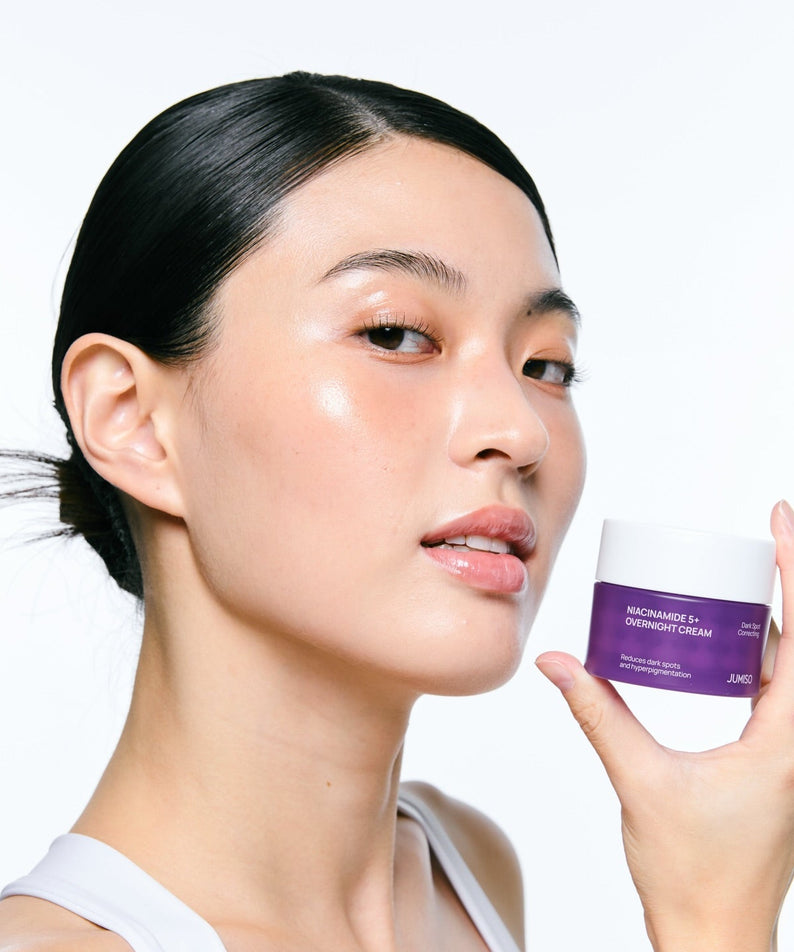 Décris l'image en français : JUMISO  Niacinamide 5 Plus Overnight Cream 80ml, femme tenant le pot, studio skincare.