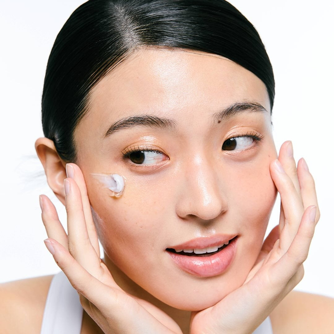 Décrivez l'image en français : JUMISO  Niacinamide 5 Plus Overnight Cream 80ml, femme applique la crème sur le visage, studio blanc.