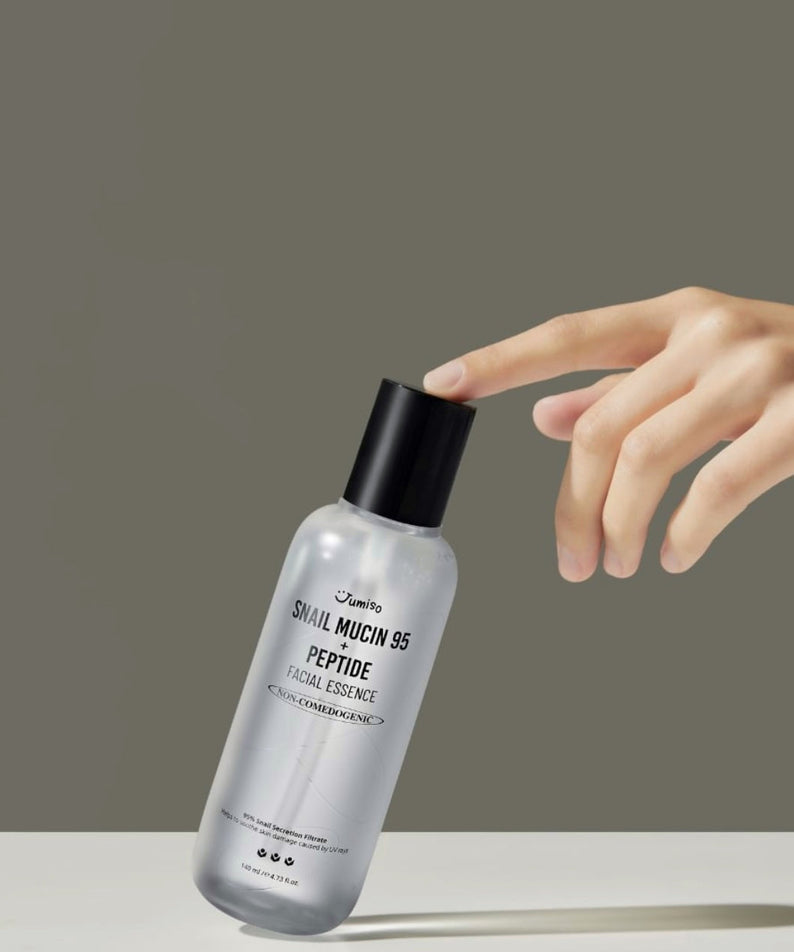 JUMISO Snail Mucin 95+ Peptide Facial Essence 140ml en bouteille transparente avec bouchon noir, main touchant le flacon.