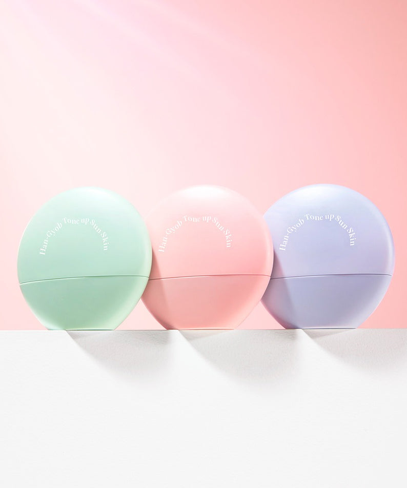 Trois pots de crème pastel sur fond rose pour KAHI One Layer Tone-up Sun Skin 40ml, soin solaire et teinté.