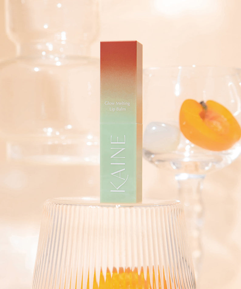 BAUME LÈVRES KAINE Glow Melting sur fond pêche translucide avec éléments décoratifs.