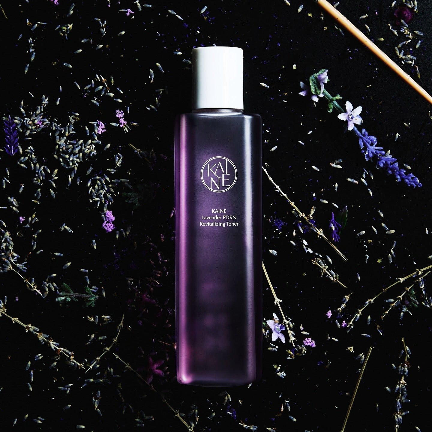 KAINE Lavender PDRN Revitalizing Toner 300ml de KAINE sur fond sombre avec fleurs de lavande et particules, produit beauté
