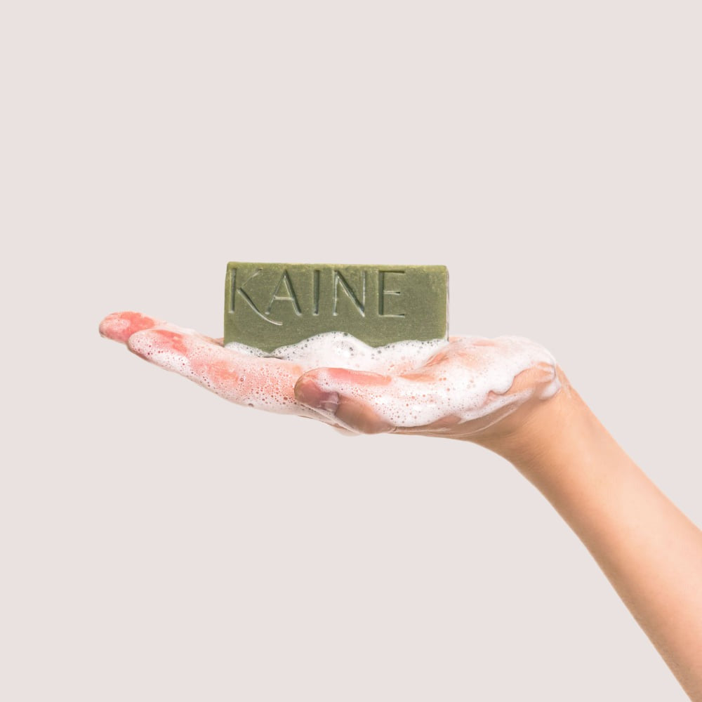 KAINE Rosemary Acne Mildly Acidic Cleansing Bar 100g, savon vert de la marque KAINE sur main, mousse, fond clair.