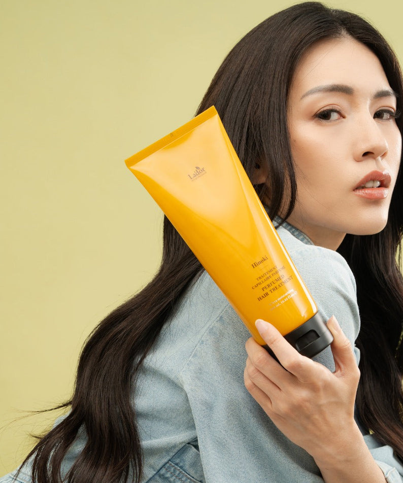 LADOR Perfume Hair Treatment 380ml : femme tenant le flacon jaune Lador, cheveux et produit sur fond clair.
