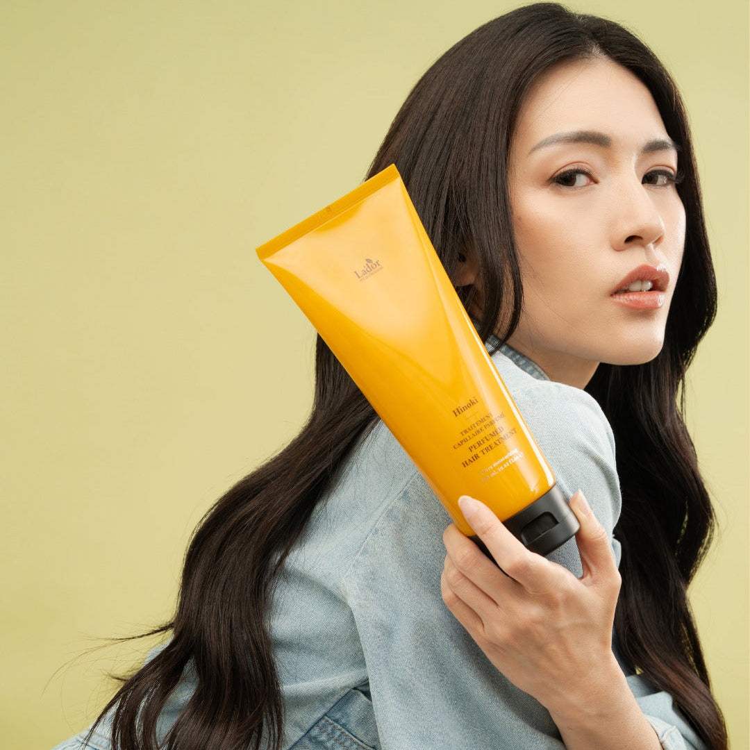 LADOR Perfume Hair Treatment 380ml : femme tenant le flacon jaune Lador, cheveux et produit sur fond clair.