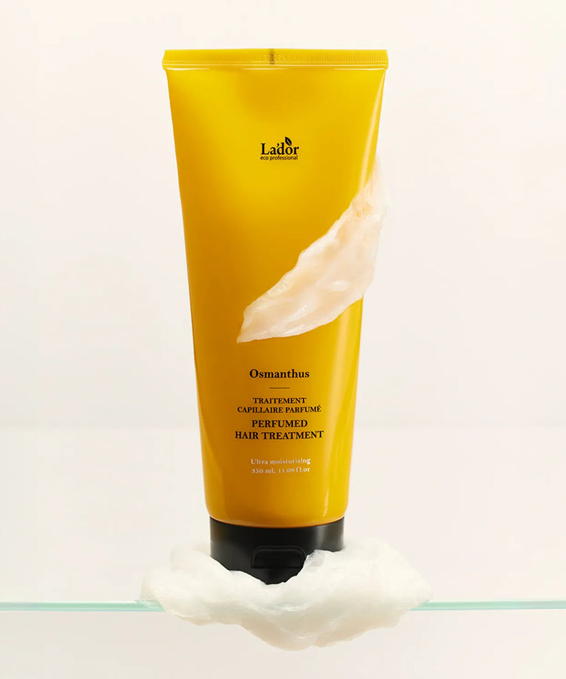 LADOR Perfume Hair Treatment 380ml de Lador, tube jaune posé sur coton, contexte blanc minimaliste.