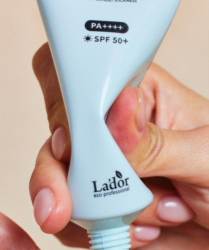 Tube de LADOR Tamanu Mild Sunscreen 50ml tenu dans une main, montrant la texture de la crème solaire SPF 50+, protection solaire douce.