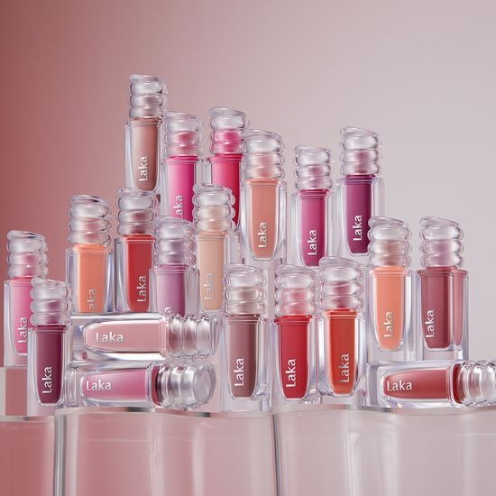 LAKA Maxi Glare Tint : tubes et flacons LAKA, vue en studio sur fond rose, ambiance maquillage brillante.