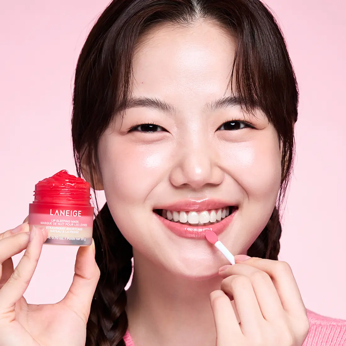 Décris l’image en français : LANEIGE Lip Sleeping Mask EX Strawberry Shortcake 20g, pot rose et femme appliquant un baume.