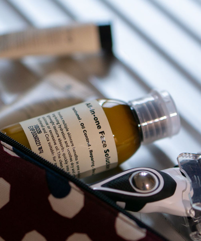 LAZY SOCIETY ALl-in-One Face Solution 50ml de la marque Lazy Society, flacon sur table avec trousse, arrière-plan bleu.