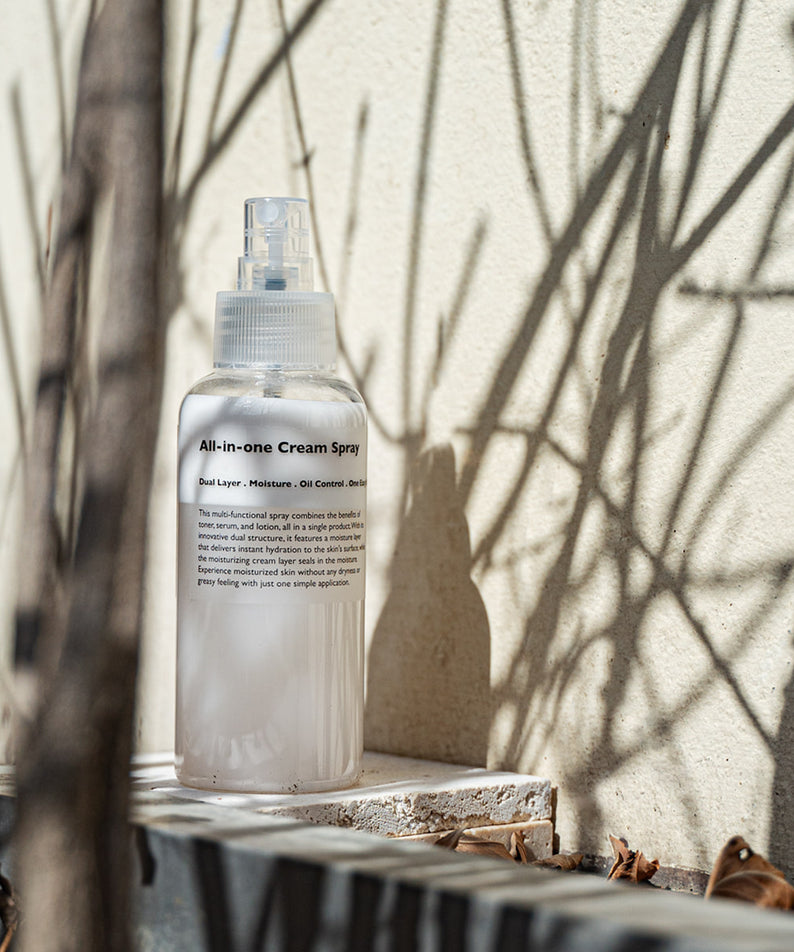 LAZY SOCIETY All-in-One Cream Spray 120ml, flacon sur table au jardin, lumière naturelle, marque en évidence.