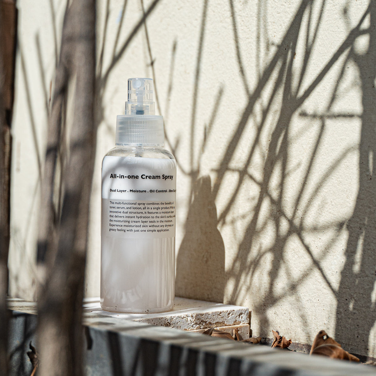 LAZY SOCIETY All-in-One Cream Spray 120ml, flacon sur table au jardin, lumière naturelle, marque en évidence.