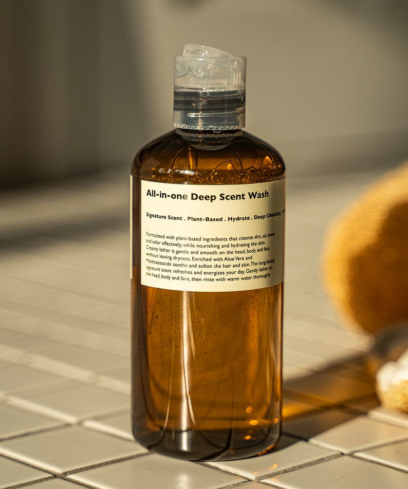 LAZY SOCIETY All-in-One Deep Scent Wash 300ml : flacon ambré sur carrelage, bain/serviettes en arrière-plan, salle de bain