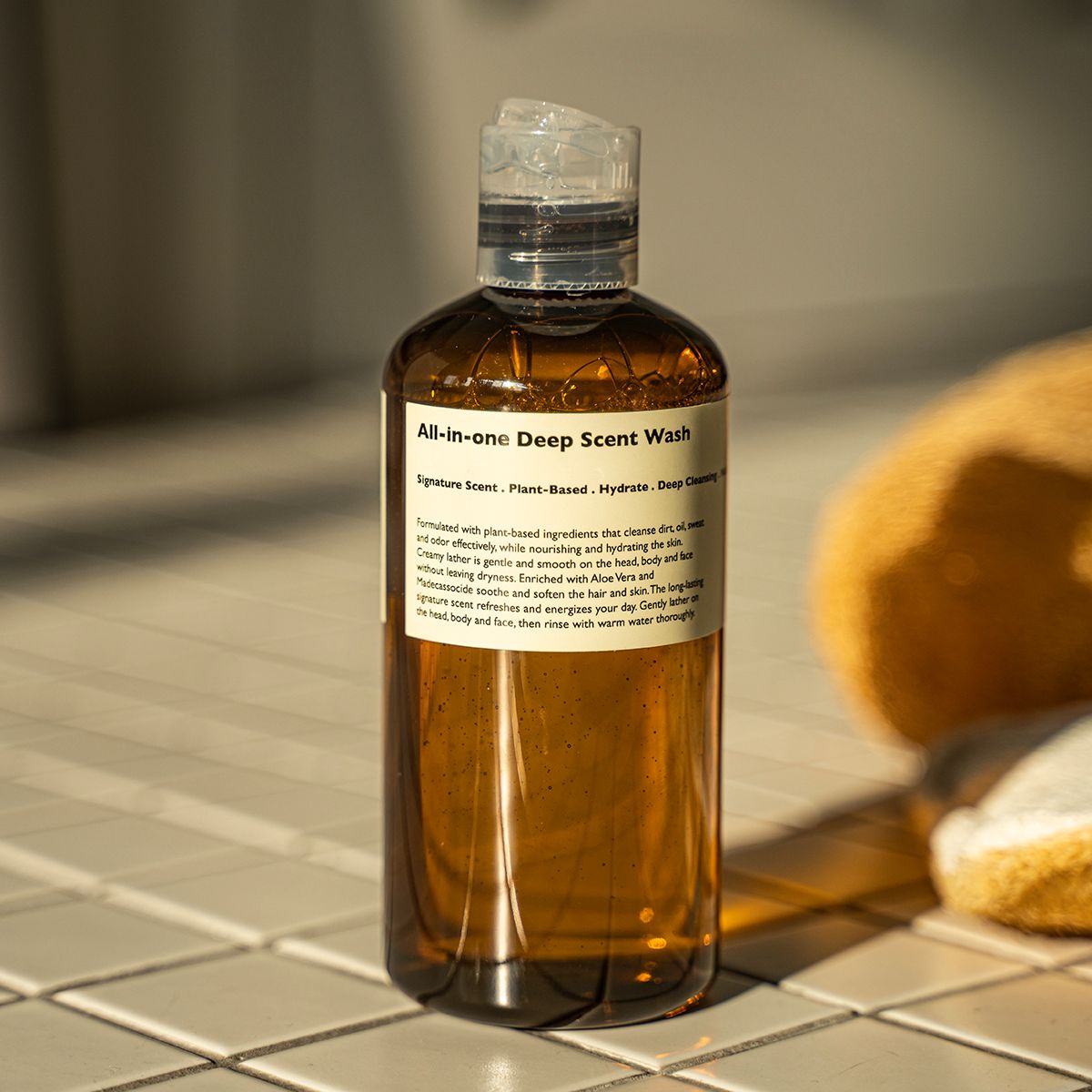 LAZY SOCIETY All-in-One Deep Scent Wash 300ml : flacon ambré sur carrelage, bain/serviettes en arrière-plan, salle de bain
