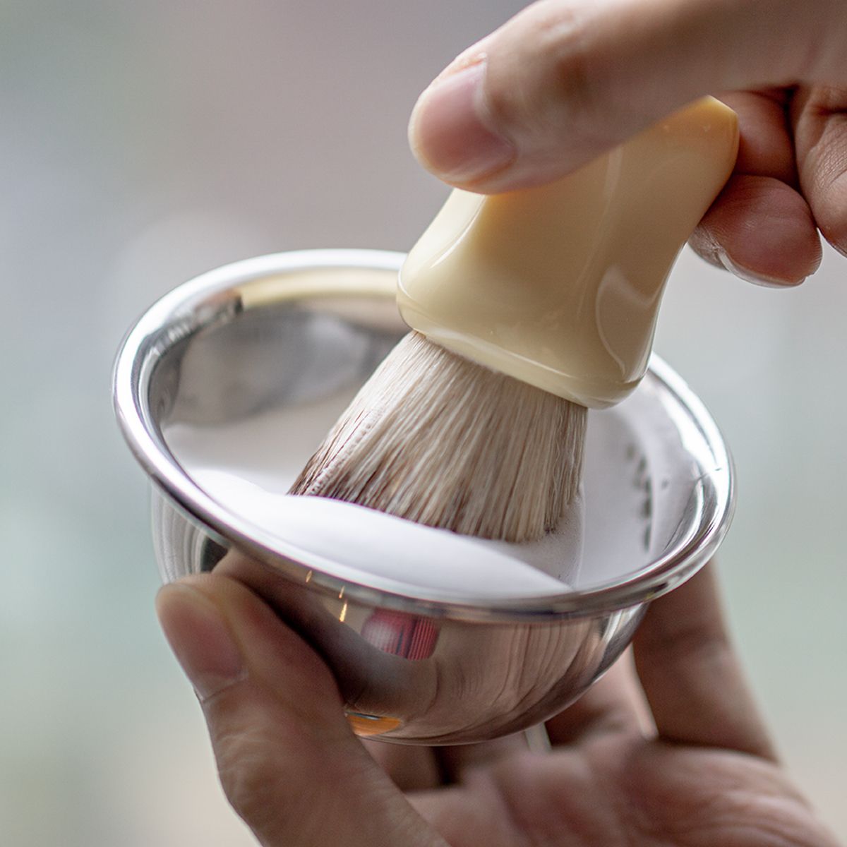 LAZY SOCIETY Classic Shaving Brush, main tenant un blaireau en mousse dans un bol d’atelier, vue rapprochée.
