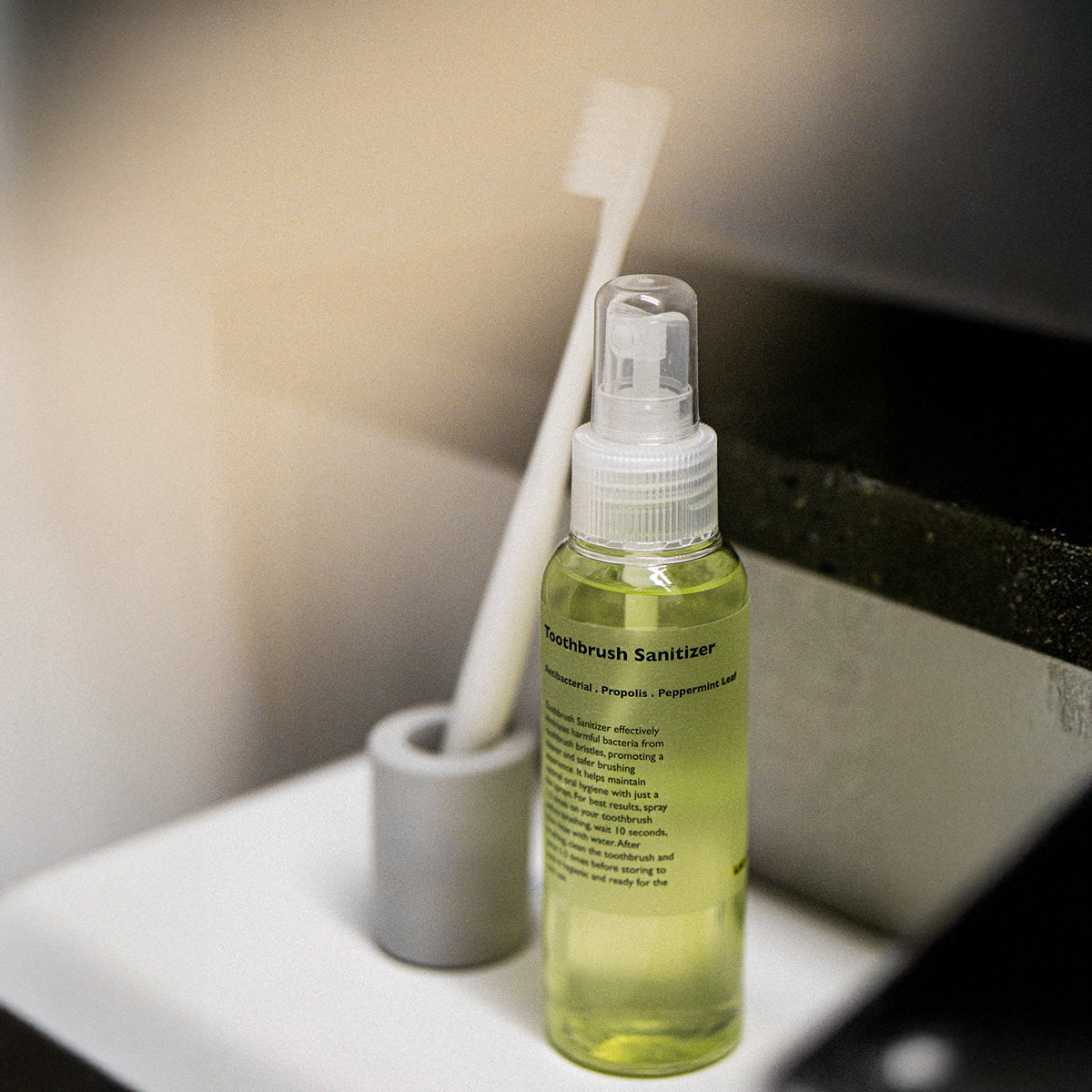 LAZY SOCIETY Toothbrush Sanitizer 100ml : flacon vert dans une salle de bain, brosse et flacon sur plan de travail.