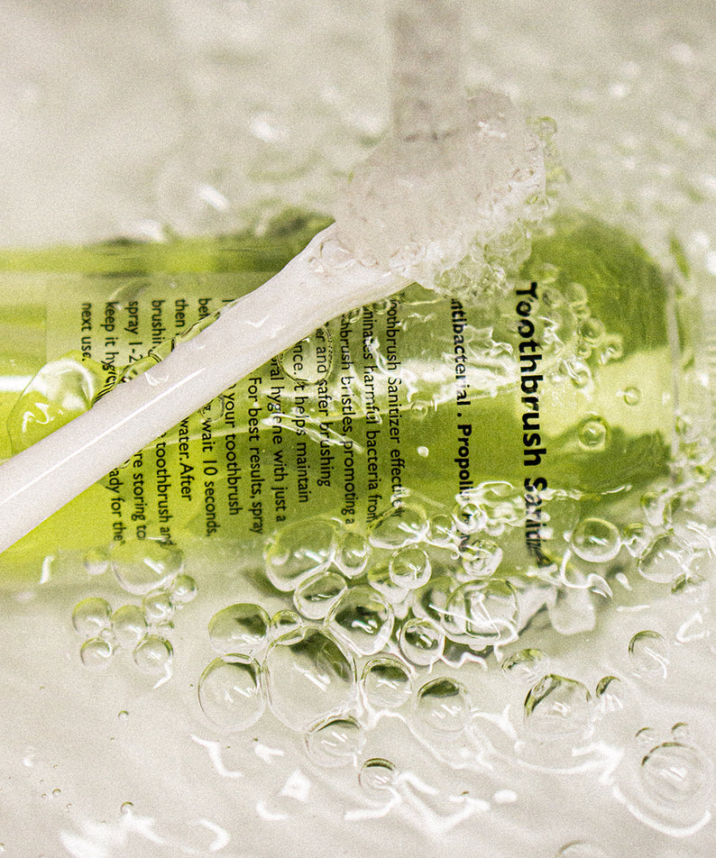 LAZY SOCIETY Toothbrush Sanitizer 100ml : vaporisation en contexte salle de bain, flacon vert sous bulles d’eau, marque visible.