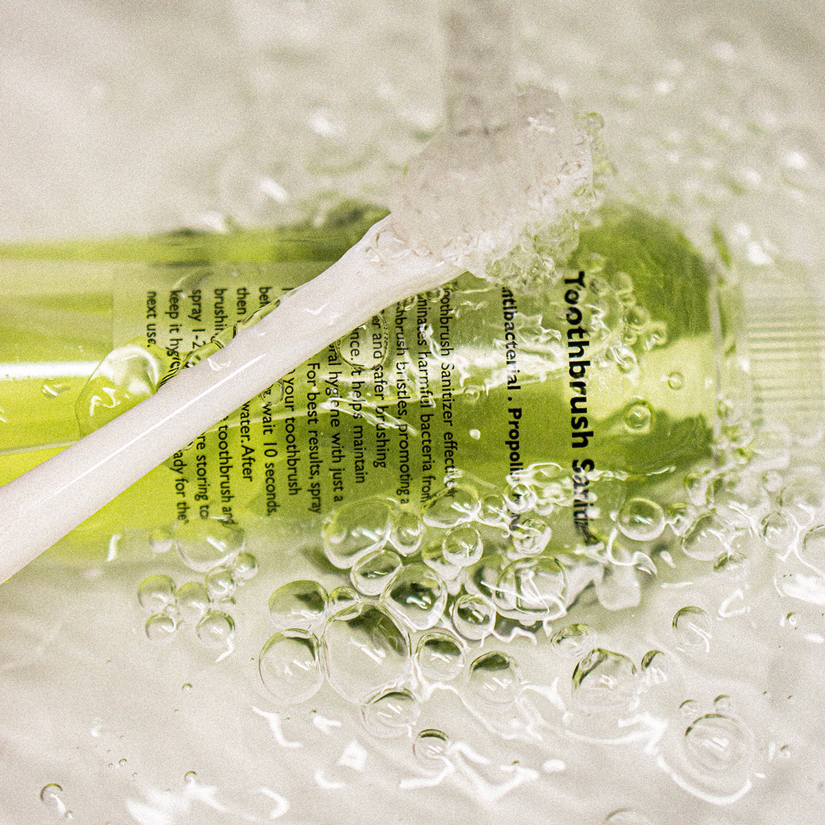 LAZY SOCIETY Toothbrush Sanitizer 100ml : vaporisation en contexte salle de bain, flacon vert sous bulles d’eau, marque visible.
