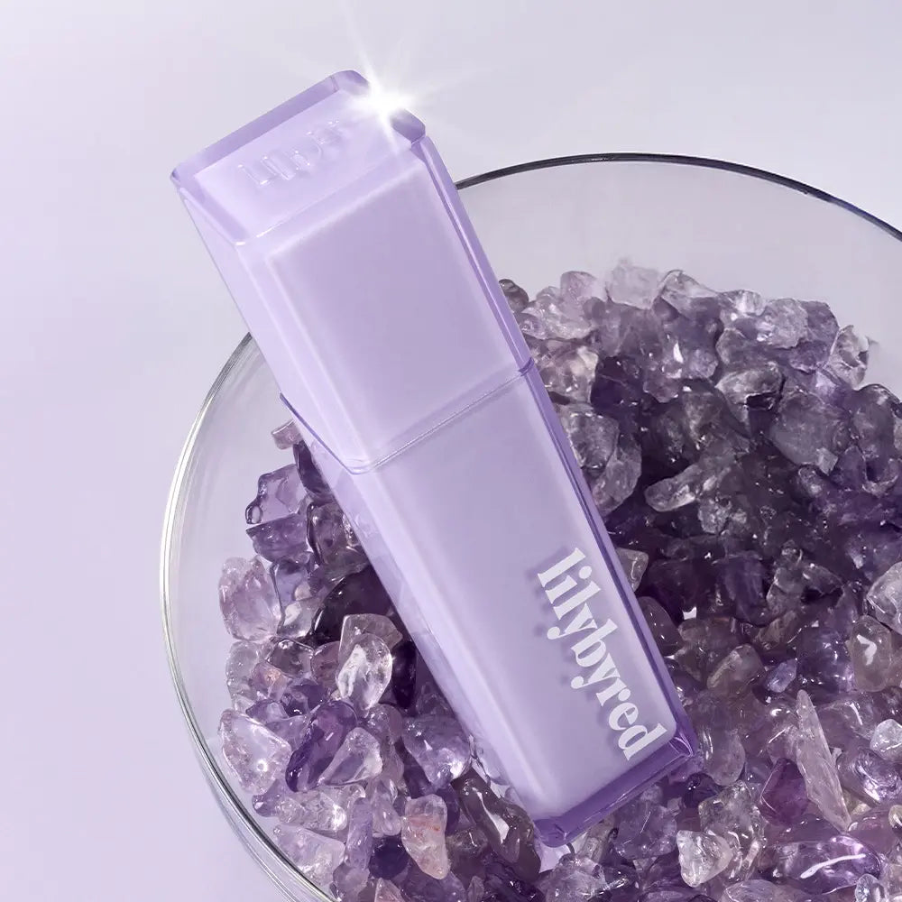 LILYBYRED Bloody Coating Tint de la marque sur fond lilas, flacon violet transparent devant des cristaux.