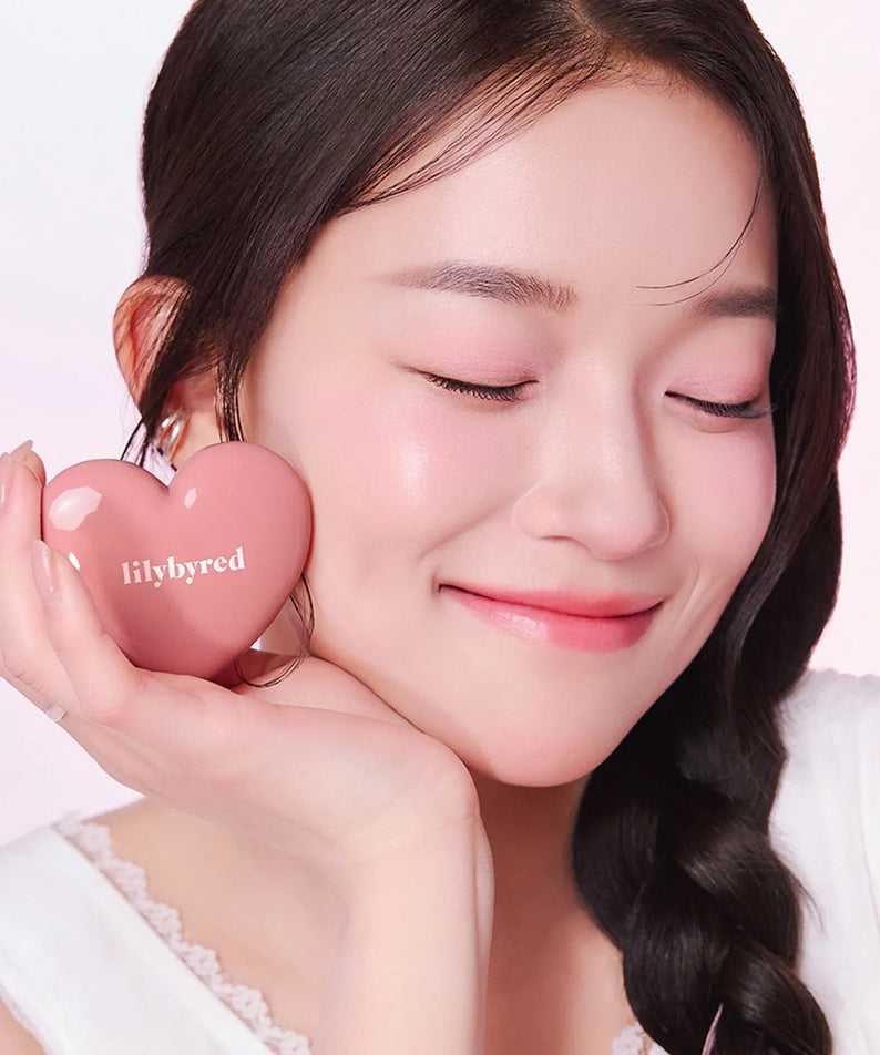 LILYBYRED Love Beam Cheek Balm de la marque LILYBYRED, femme au maquillage appliqué, flacon en forme de cœur rose