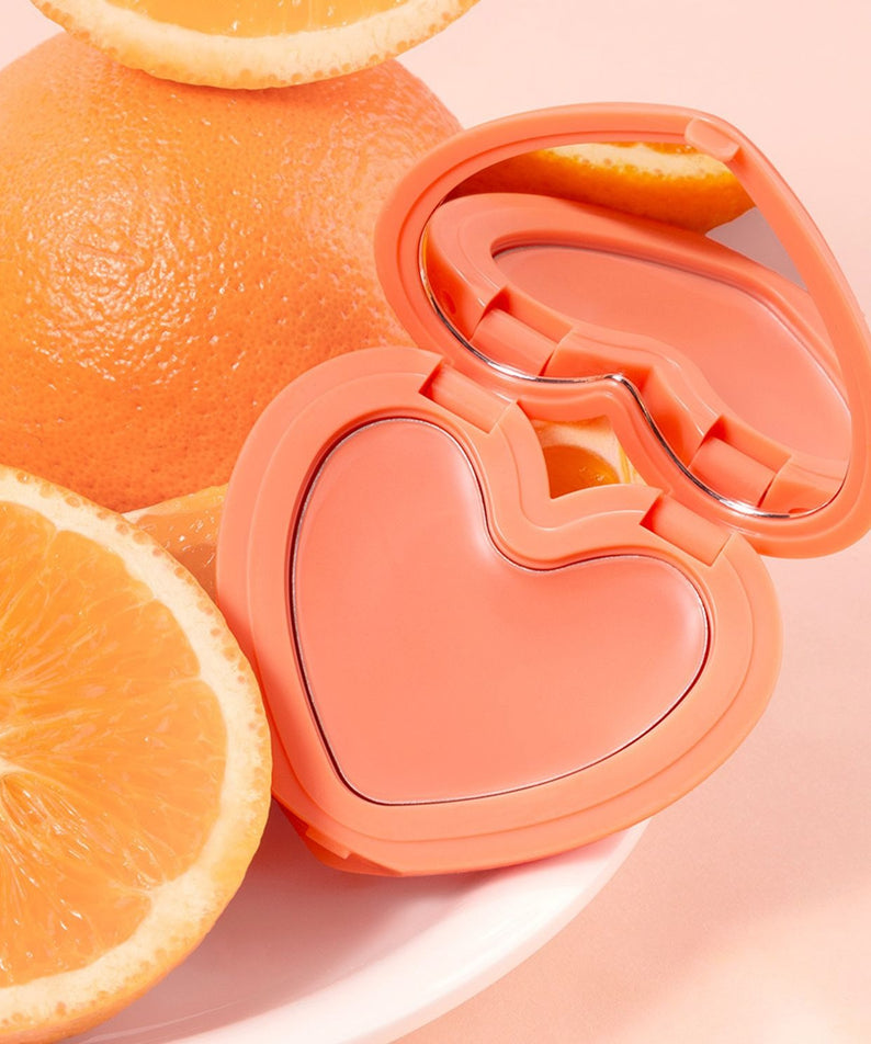Décris l'image en français en mentionnant LILYBYRED Love Beam Cheek Balm, marque LILYBYRED, boîtier et agrumes, fond rose pastel.