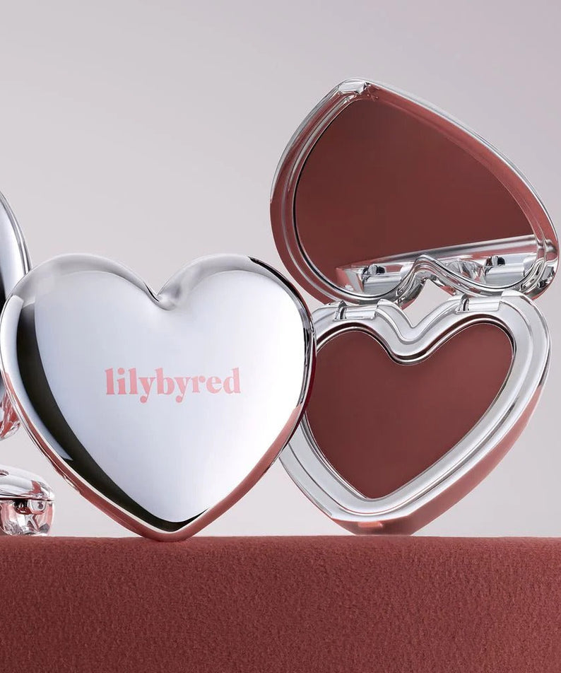 LILYBYRED Love Beam Cheek Mousse, marque lilybyred, packaging cœur argenté sur fond rose, maquillage blush.