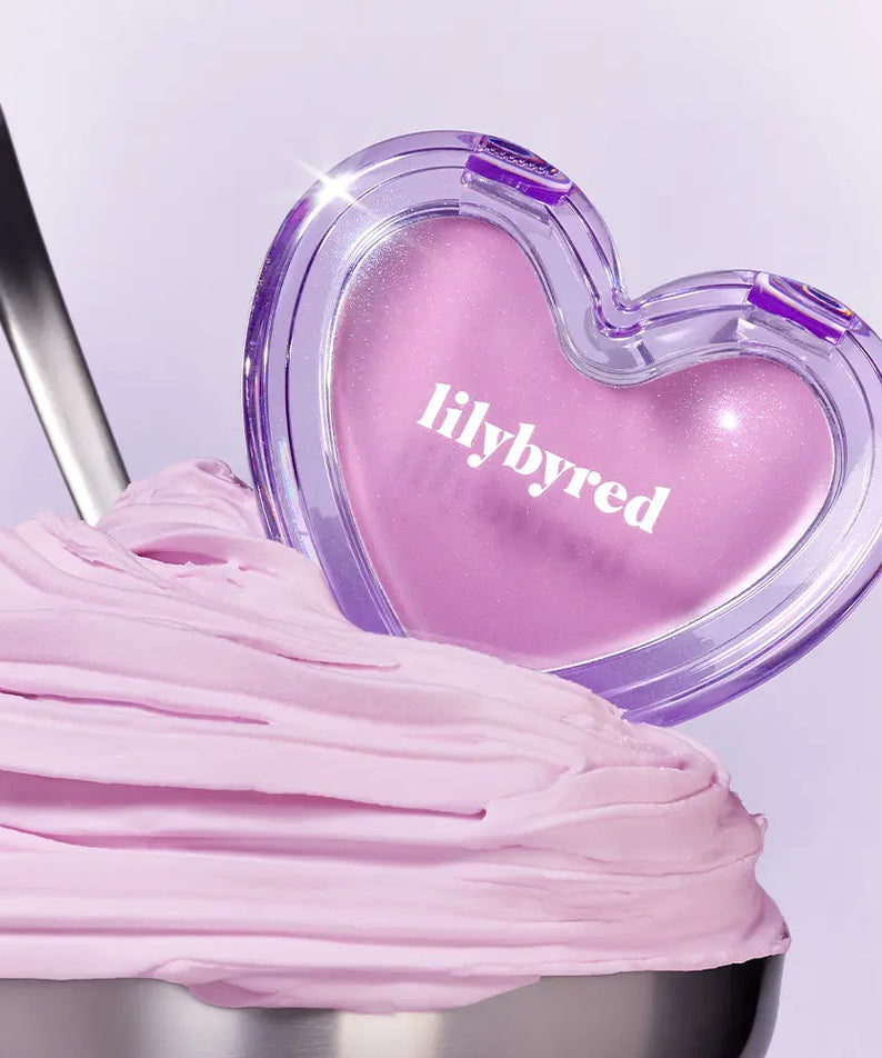 Décris l'image en français : LILYBYRED Love Beam Sherbet Cheek, marque LILYBYRED, flacon cœur violet sur fond pastel, maquillage