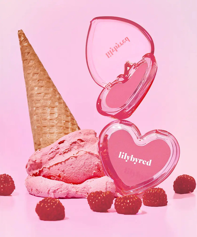 Décris l’image en français : LILYBYRED Love Beam Sherbet Cheek, marque LILYBYRED, blush rose liquide sur fond rose, cône glace et framboises.