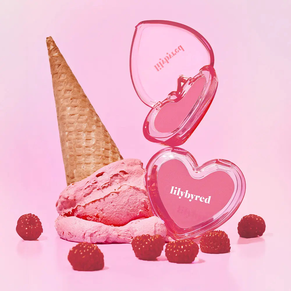 Décris l’image en français : LILYBYRED Love Beam Sherbet Cheek, marque LILYBYRED, blush rose liquide sur fond rose, cône glace et framboises.