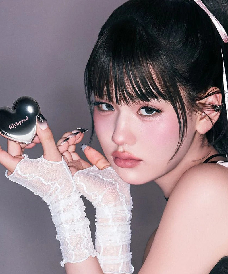 Femme utilisant le LILYBYRED Love Beam Cheek Mousse, un produit cosmétique pour les joues, avec un design de cœur élégant.