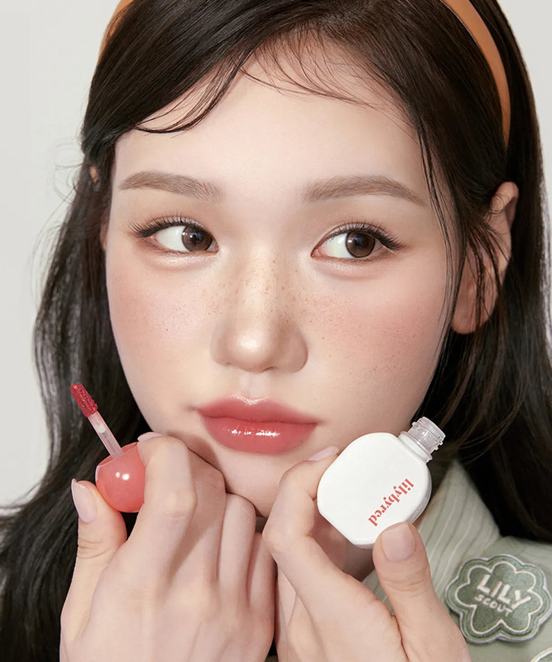 Femme appliquant LILIBYRED Sugar Wrapping Tint Gloss sur les lèvres, produit de beauté chic et tendance pour une finition brillante.