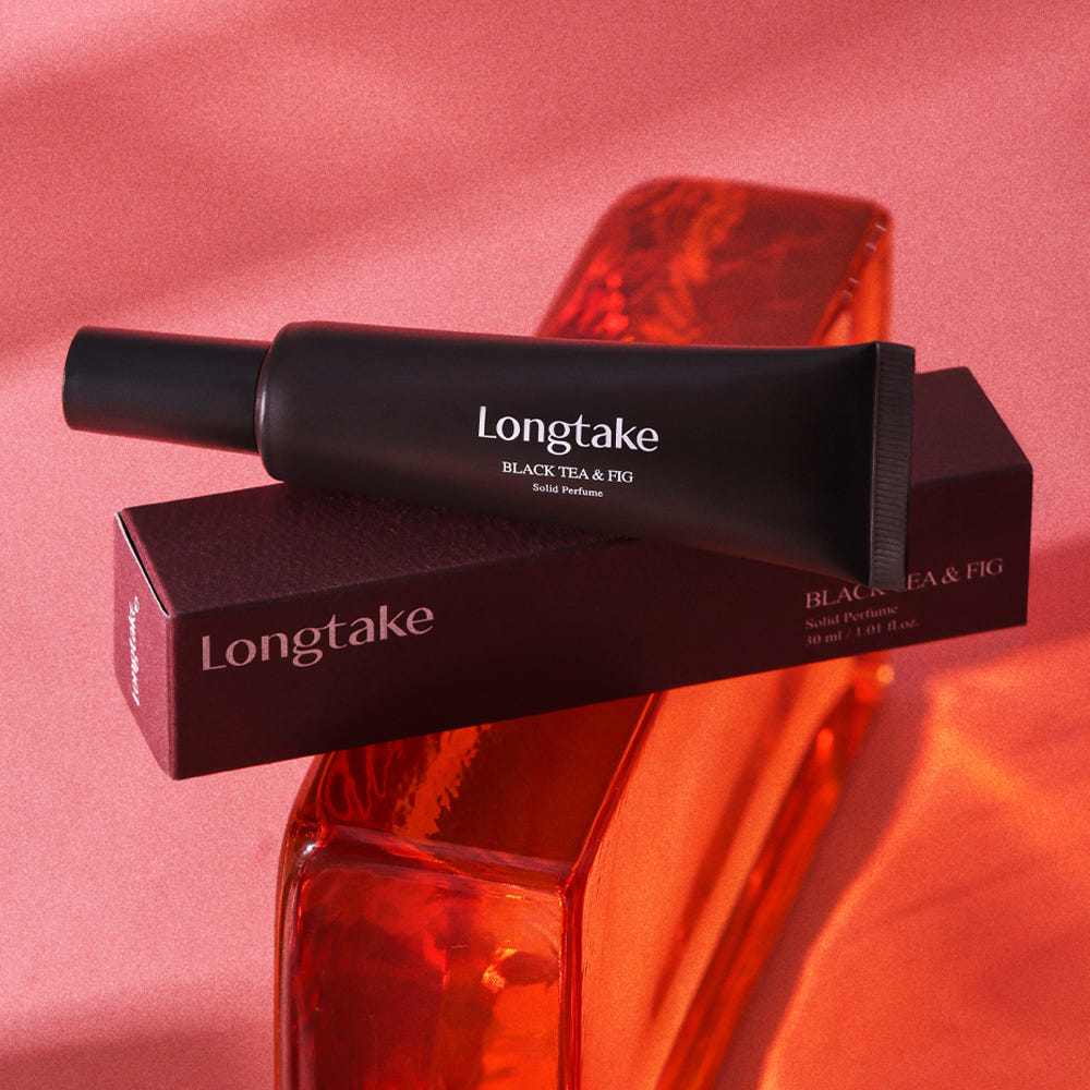 LONGTAKE Solid Perfume 30ml : tube et étui sur fond rose, bouteille & figue, produit en contexte visuel.