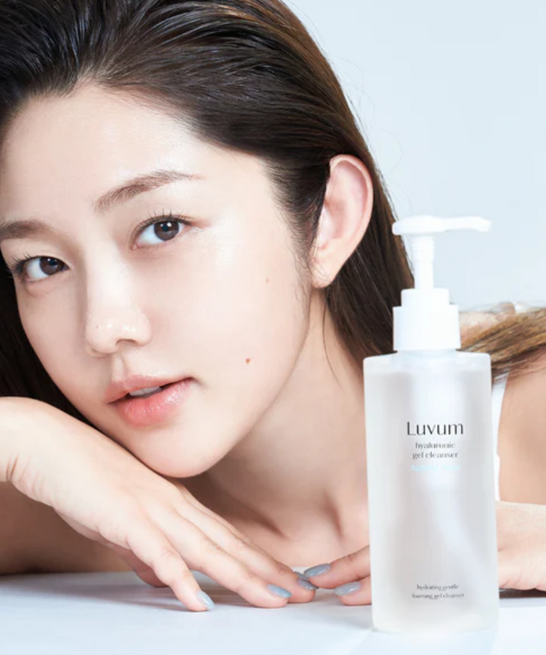 Décris l'image en français : LUVUM Bamboo Hyaluronic Acid Moisture Gel Cleanser 200ml, flacon blanc sur table, femme visage.