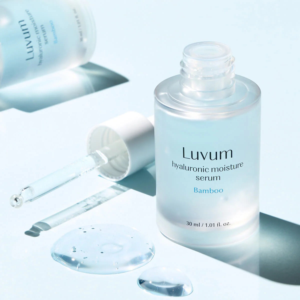 Décris l'image en français : LUVUM Bamboo Hyaluronic Acid Moisture Serum 30ml, flacon bleu sur fond lumineux, gouttes et seringue.
